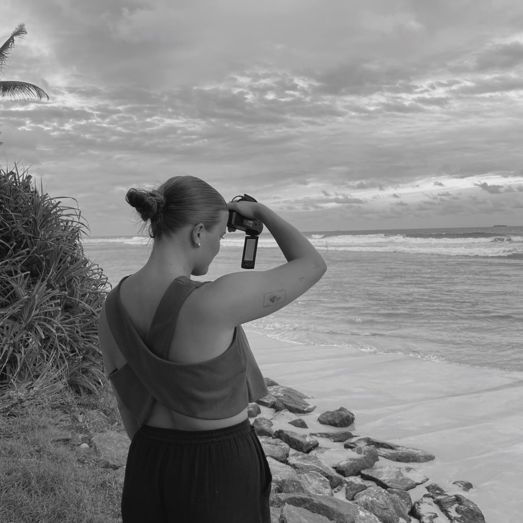 Girl with her back to the camera, recording the ocean with a camcorder