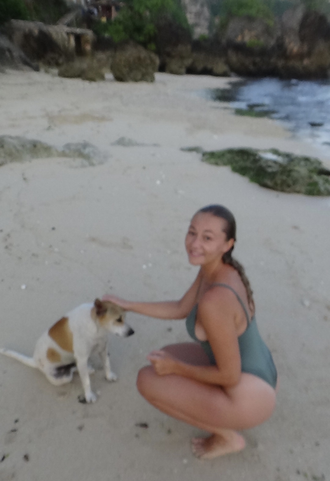 Girl petting a dog on the beach, smiling at the camera