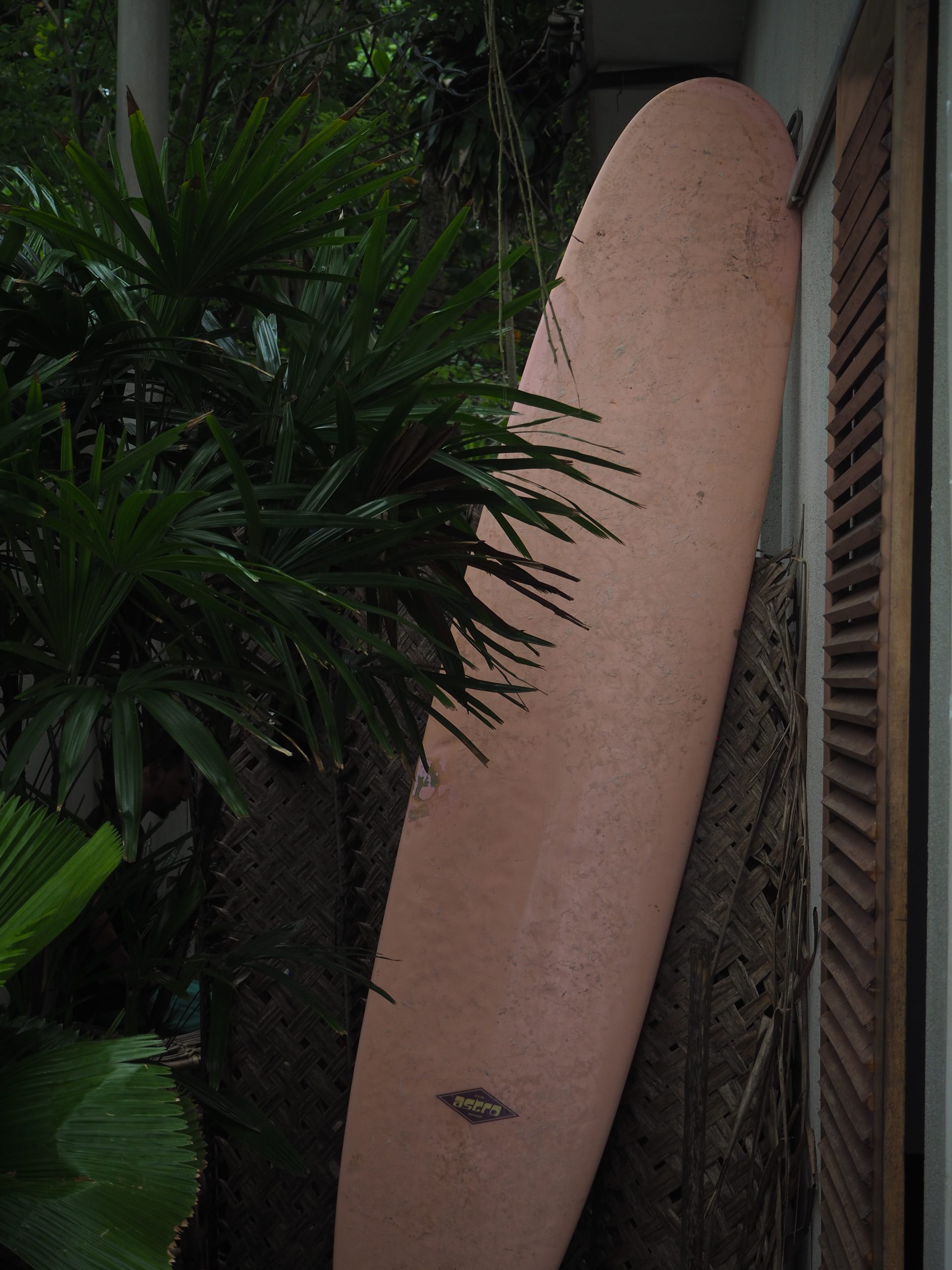 Pink surfboard leaning against a wall.