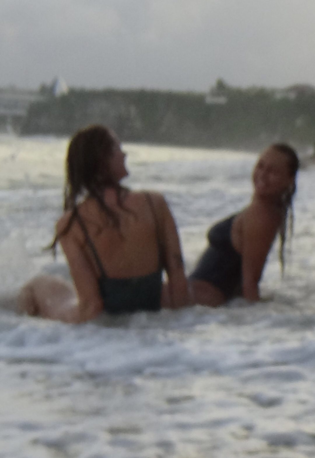 Two girls sitting on the beach in Bali, laughing as waves splash around them